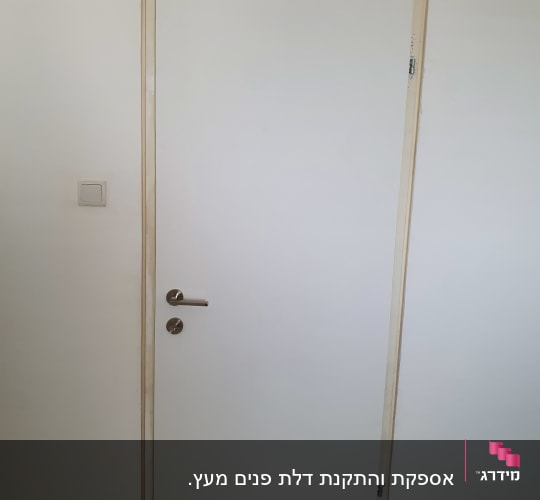 דלת לבנה עם ידית מתכת על קיר לבן
